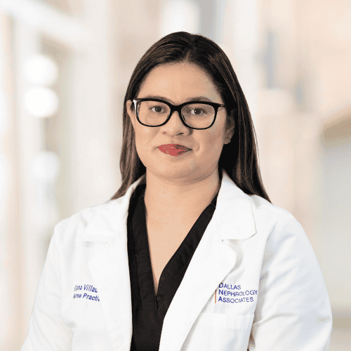 A woman wearing glasses and a white lab coat with the embroidered text "Dallas Nephrology Associates" stands against a blurred indoor background. Eliana Villado, APRN, FNP-C has long dark hair, a confident expression, and is dressed in a black top under her lab coat.