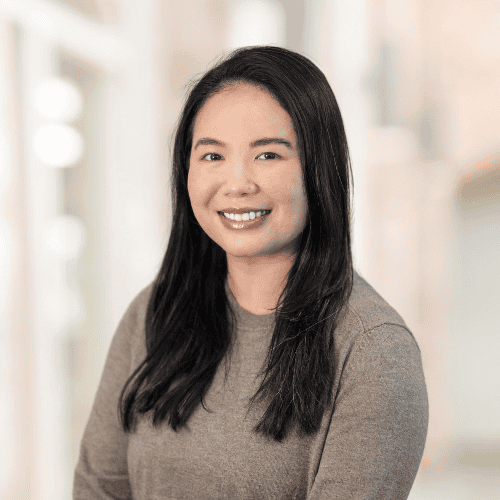 A woman with long black hair and a friendly smile, identified as Nina Rico, FNP-C, APRN, is wearing a beige sweater. She is posing against a softly blurred indoor background, creating a professional and approachable atmosphere.